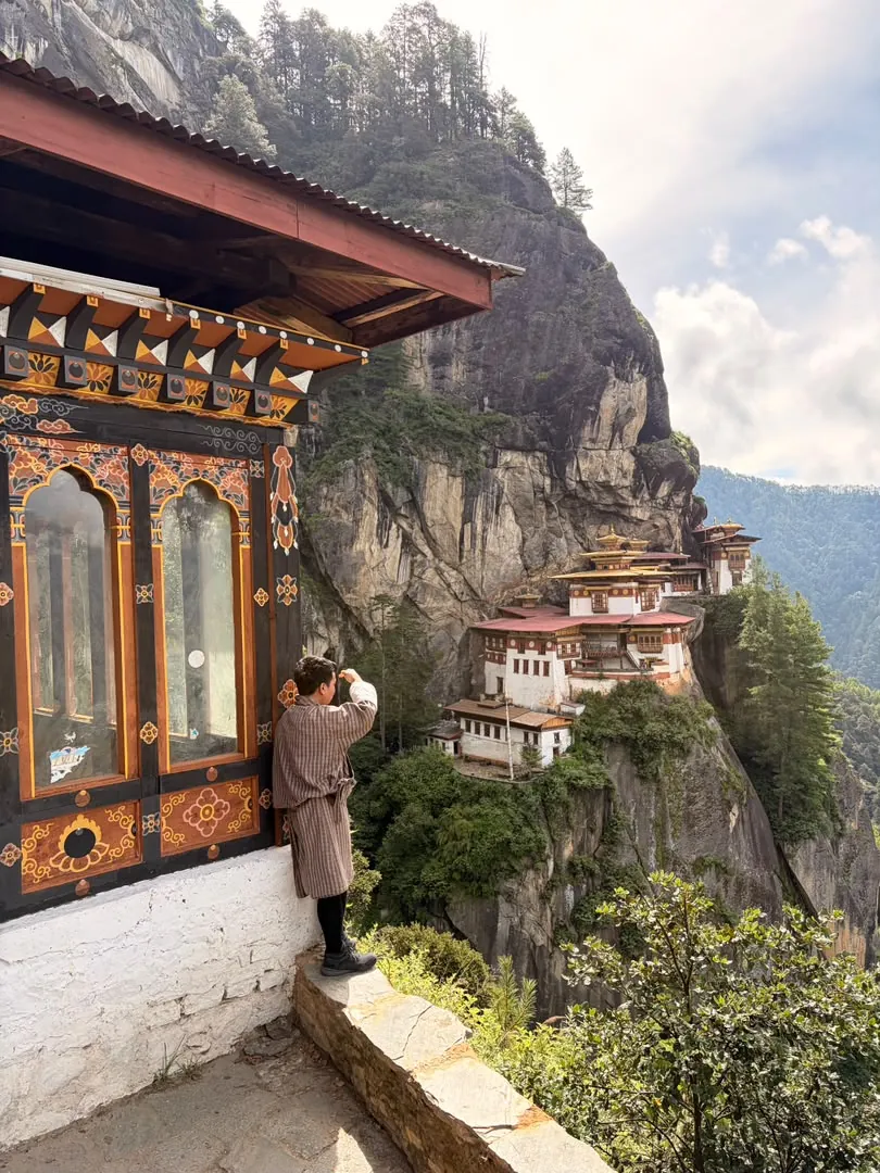 Tashi in a gho at a temple window, looking across at the Tiger's Nest monastery on the cliff