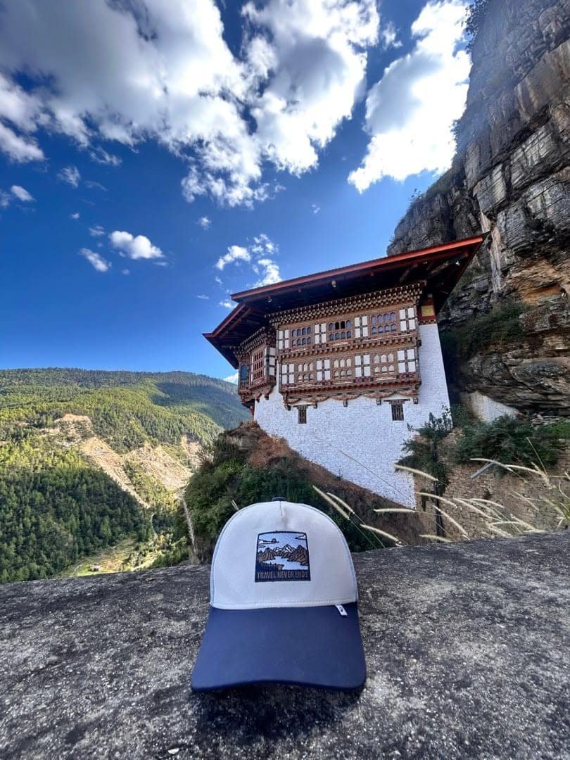 A whitewashed Bhutanese temple on a cliff under a blue sky, with a cap resting on the rock in front